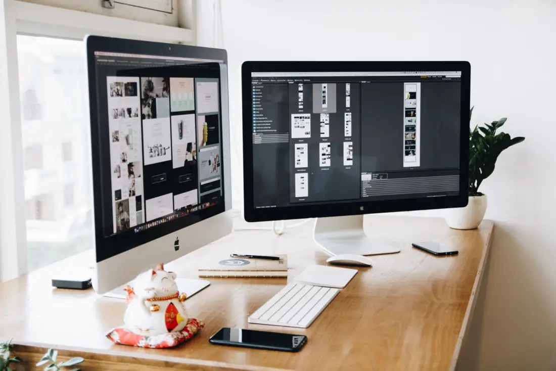 Two monitors showing website and landing page designs in a design app
